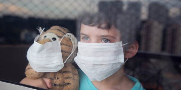 Child and Toy both wearing face coverings looking out of a window