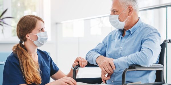 patient in wheelchair with facemask with nurse on knees in facemask talking to him