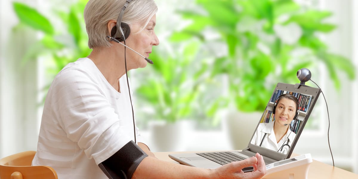 Woman with blood pressure monitor on her arm talking to doctor in web meeting