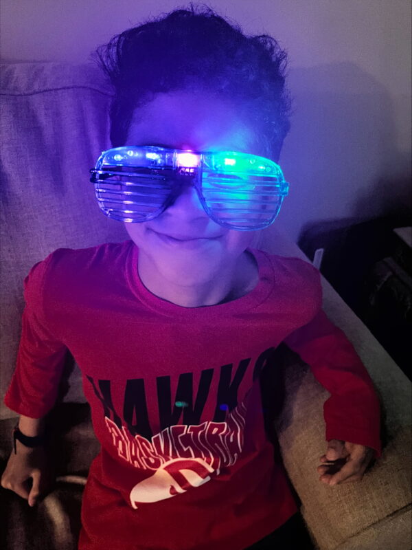 A young boy smiling with red shirt and plastic glasses that have colourful lights added to them