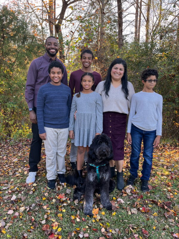 A family of 6 with parents and 4 children and a black pet dog in the forest